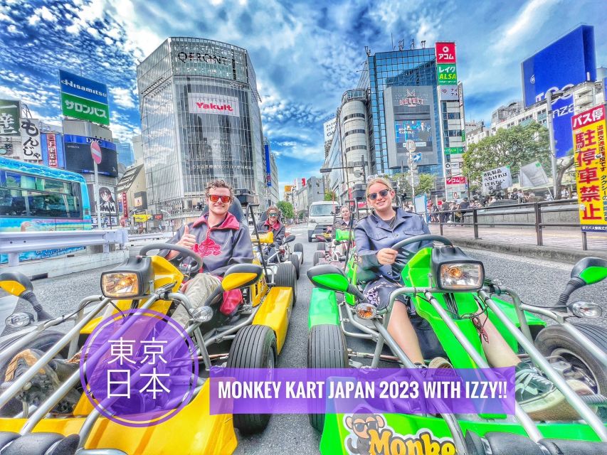 A small group of tourists drive brightly colored go karts through Akihabara on a sunny day. The camera angle angle is slightly distorted as if taken with a fisheye lens.